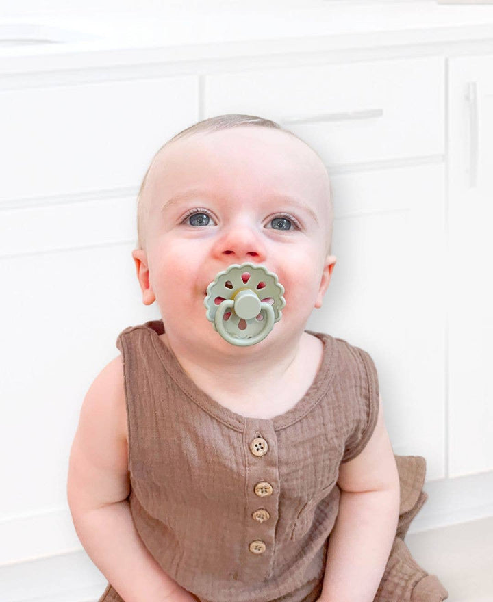 Baby wearing a brown outfit with a green pacifier against a white background
