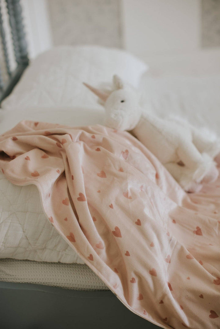 White unicorn toy on a pink blanket with heart patterns on a white surface