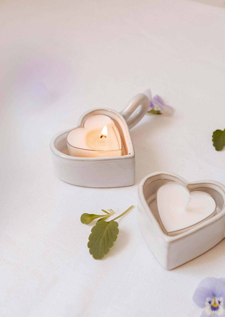 Heart-shaped ceramic candle holders with candles on a light background