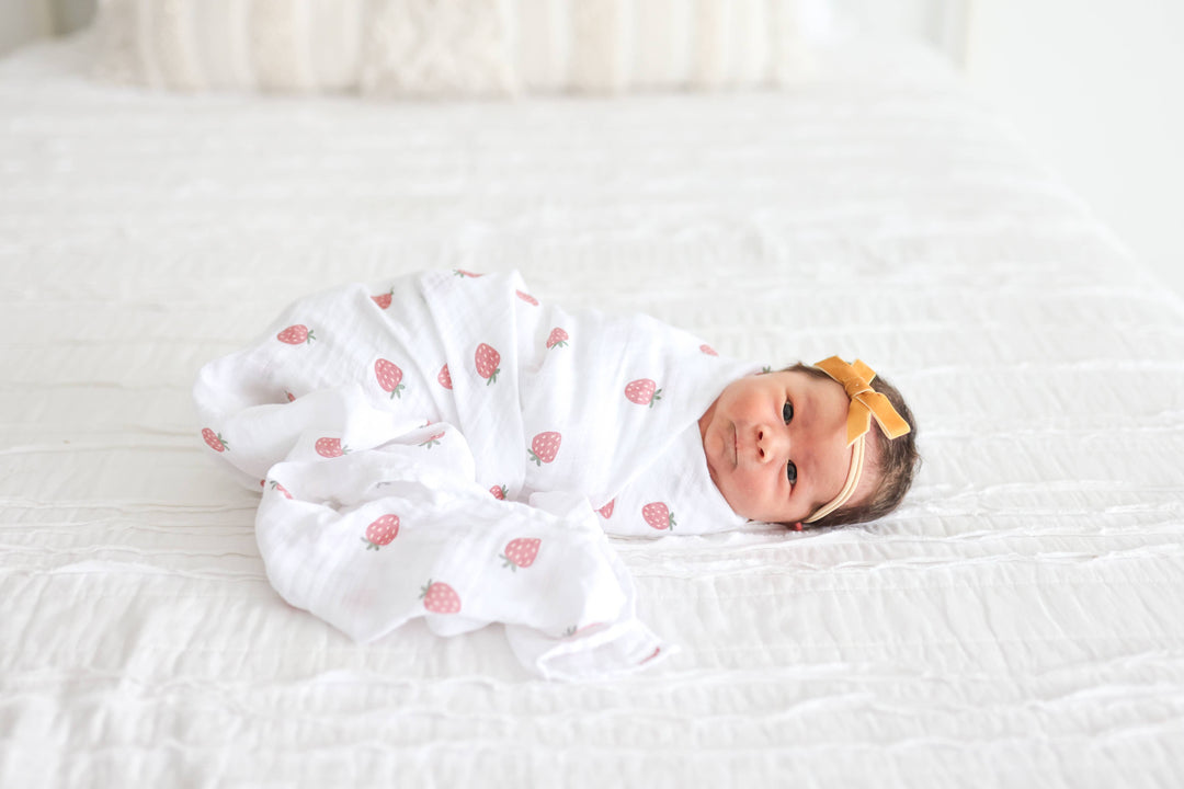 Two Lulujo Baby cotton swaddle blankets, one with strawberry print and one with ballet slipper design, laid flat on a neutral background.