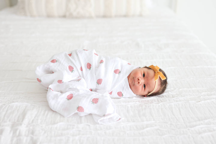 Two Lulujo Baby cotton swaddle blankets, one with strawberry print and one with ballet slipper design, laid flat on a neutral background.