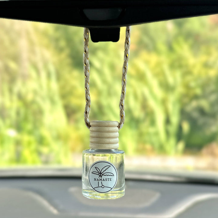 Car air freshener hanging from a rearview mirror with a blurred green outdoor background