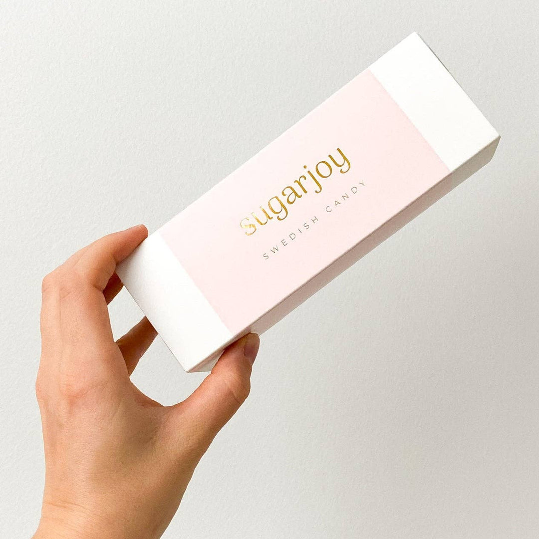 Hand holding a box of sugarjoy Swedish candy against a light gray background
