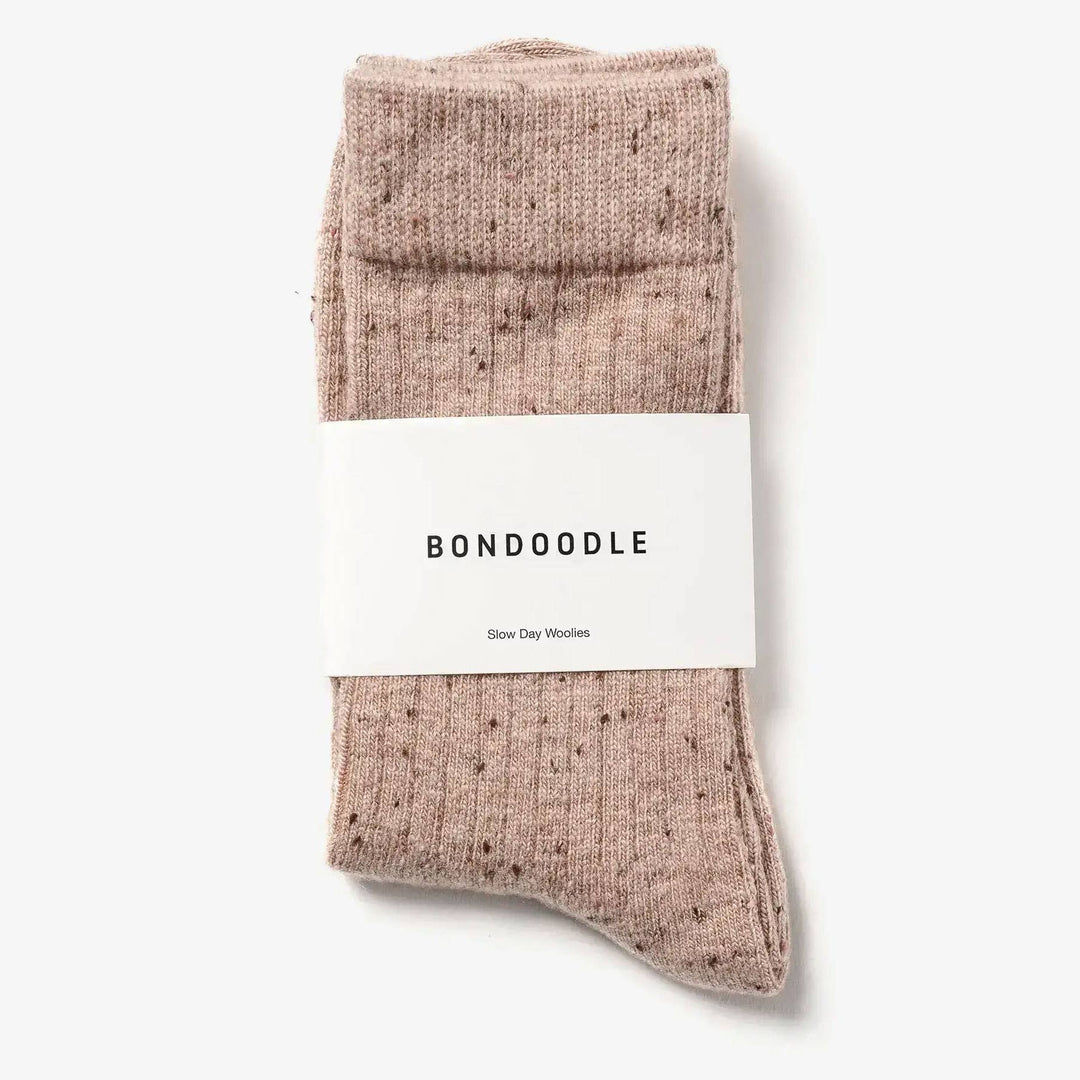 A pair of folded ribbed knit socks in a dusty rose pink color with tiny dark speckles, wrapped in a white paper band labeled &