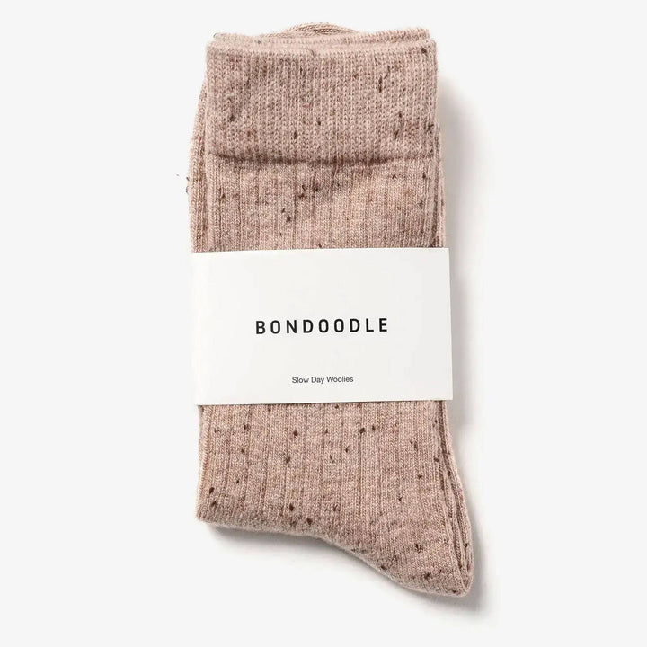 A pair of folded ribbed knit socks in a dusty rose pink color with tiny dark speckles, wrapped in a white paper band labeled &