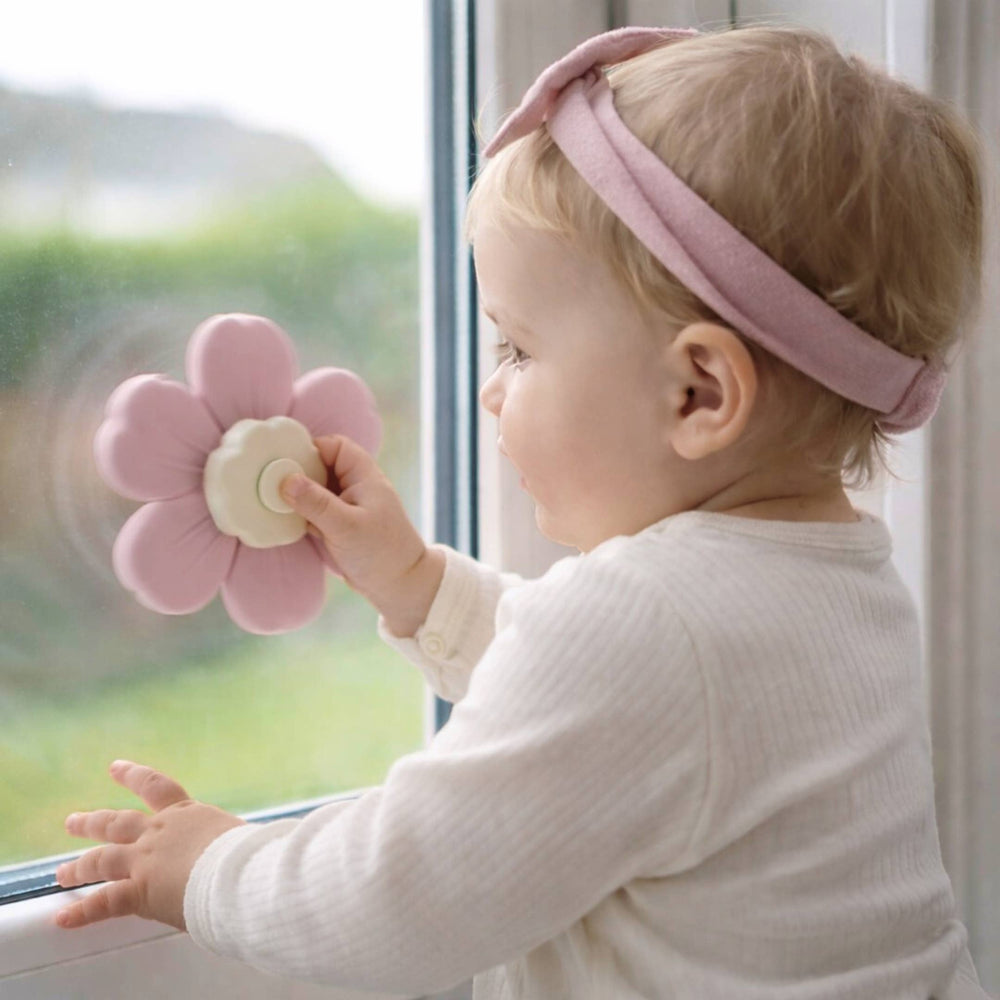 Baby holding a pink flower-shaped object by a window