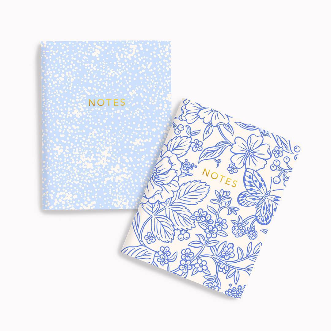 Two notebooks with floral and butterfly design on one and blue glittery design on the other, on a white background.