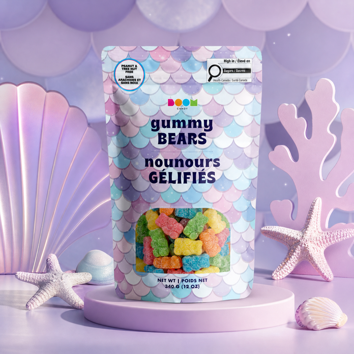 A stand-up pouch of Boom Bunnies Gummy Bears candy, decorated with a pastel mermaid scale pattern, displayed on a lavender pedestal with seashell and starfish props in a purple-themed setting.