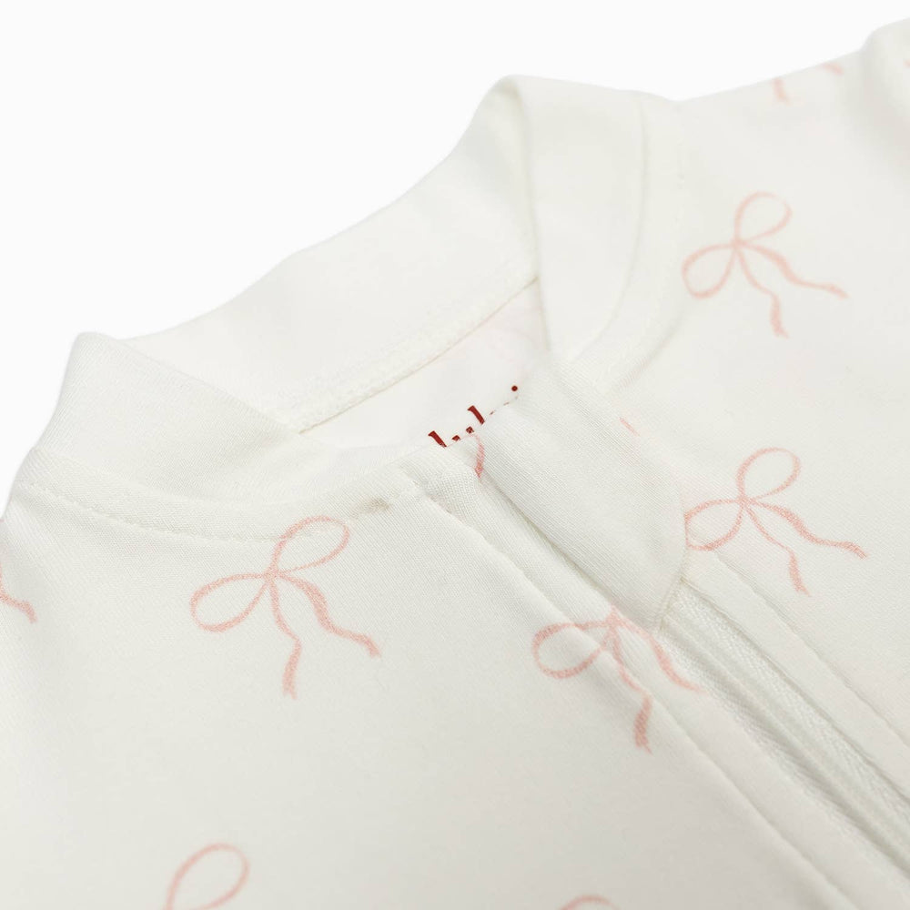 Close-up of a white or off-white garment with a soft pink bow pattern and a zipper detail, photographed on a clean white background.