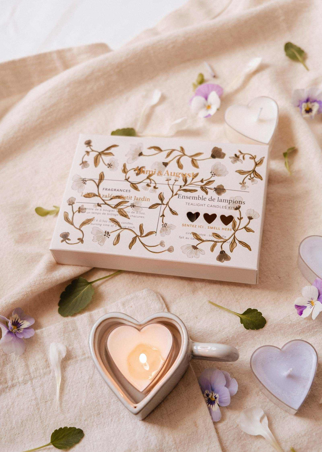 Heart-shaped candle holder with a lit candle on a beige fabric background with flowers.