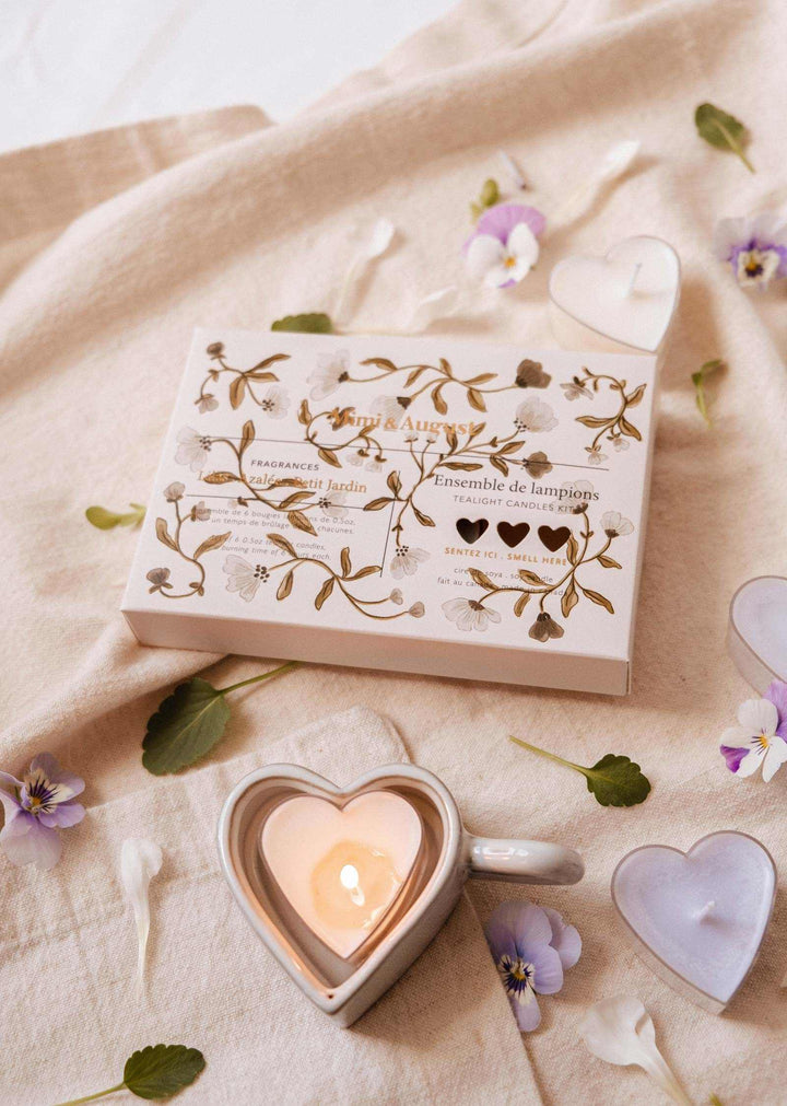 Heart-shaped candle holder with a lit candle on a beige fabric background with flowers.