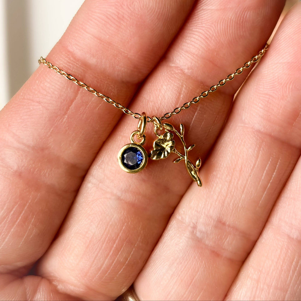 Gold necklace with a blue gemstone pendant held between fingers