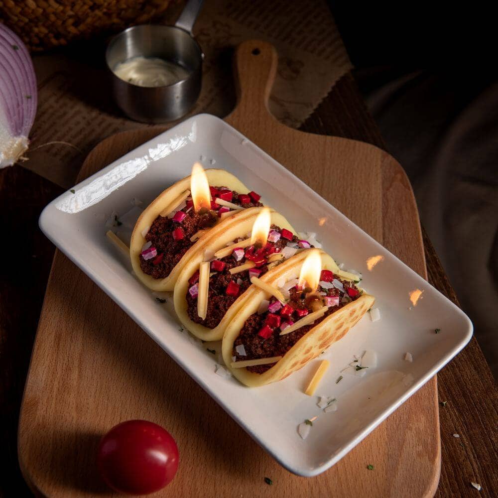 Three tacos on a white plate with flames, placed on a wooden surface.