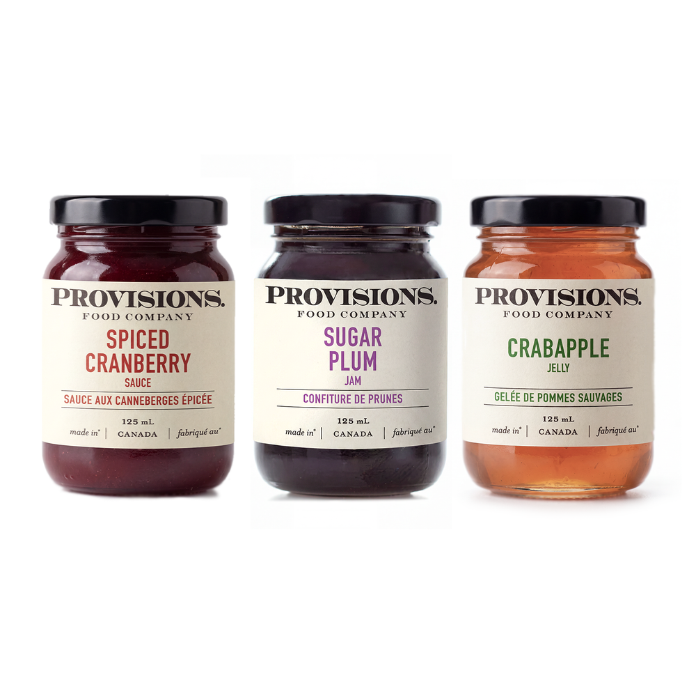 Assorted jars of Provisions Food Company Holiday Collection jams and jellies with colorful labels and festive packaging.