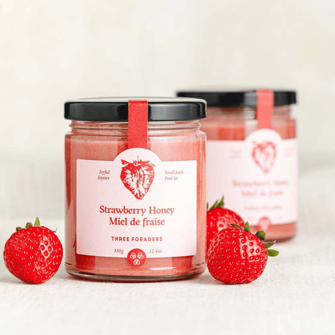Jar of strawberry infused honey by Three Foragers, 350g, showing the honey with fresh strawberry pieces inside.