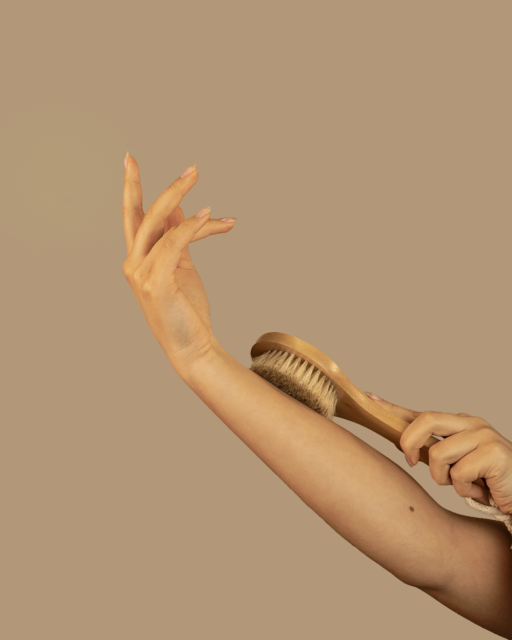 Person using a wooden brush on their arm against a beige background