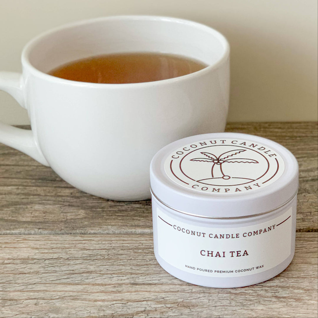 White mug with tea and a container of Chai Tea from Coconut Candle Company on a wooden surface.