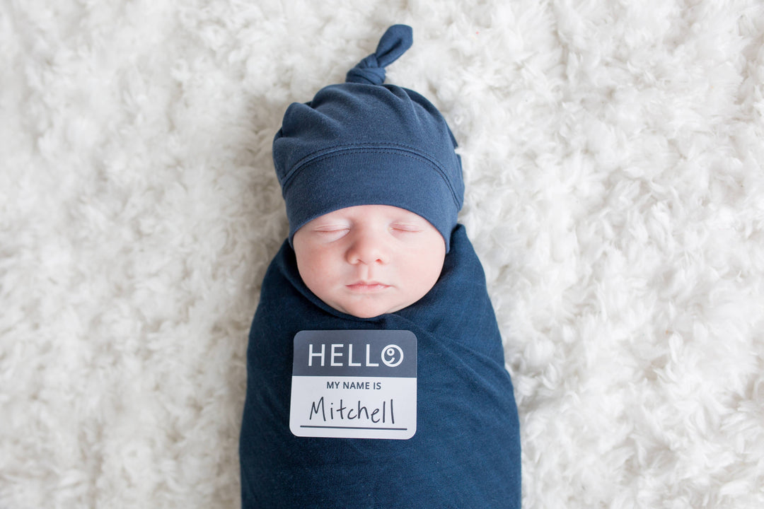 Newborn baby wrapped in blue swaddle with a name tag on a white background