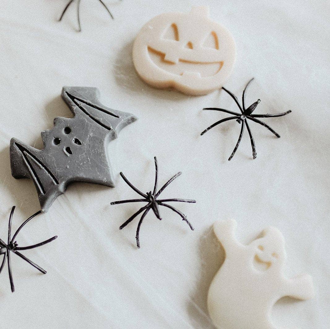 Halloween-themed cookie cutters or stamps on a white surface, including a gray bat, a cream pumpkin, a cream ghost, and several black spider designs.