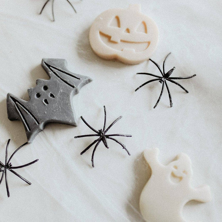 Halloween-themed cookie cutters or stamps on a white surface, including a gray bat, a cream pumpkin, a cream ghost, and several black spider designs.
