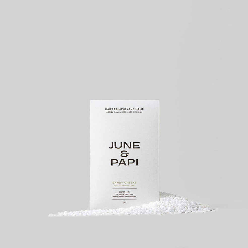 A white rectangular box labeled 'JUNE & PAPI' stands upright on a light gray background, with a small pile of white granules in front of it.