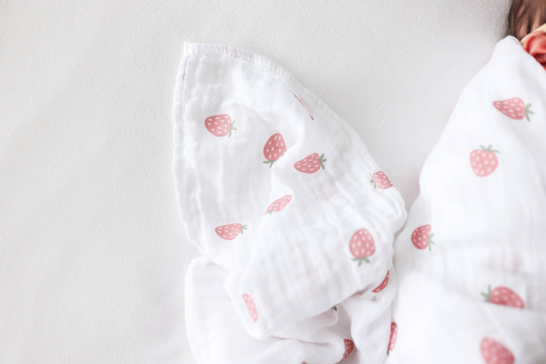 Two Lulujo Baby cotton swaddle blankets with strawberry and ballet slipper patterns, soft and breathable for infants.