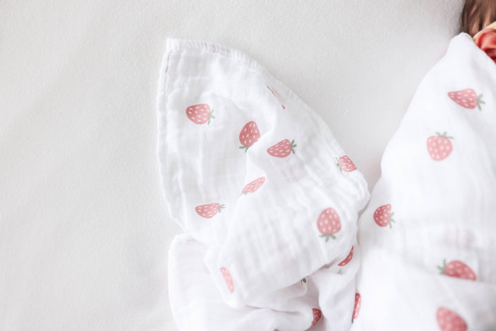 Two Lulujo Baby cotton swaddle blankets with strawberry and ballet slipper patterns, soft and breathable for infants.
