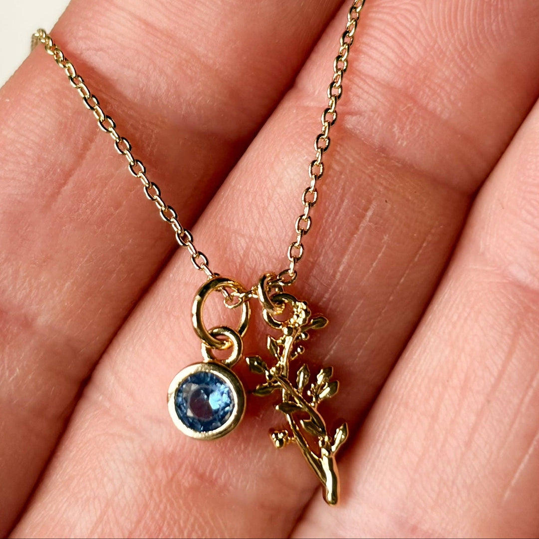 Gold necklace with a blue gemstone pendant held between fingers