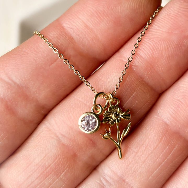 Gold necklace with a pendant held in a hand against a neutral background