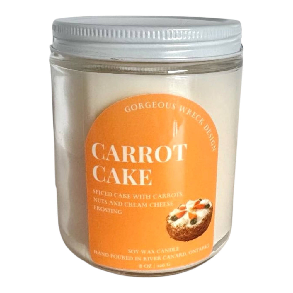 An 8 oz soy wax candle in a clear glass jar with a white screw-on lid and a prominent orange label reading 'CARROT CAKE' with a small carrot cake illustration.