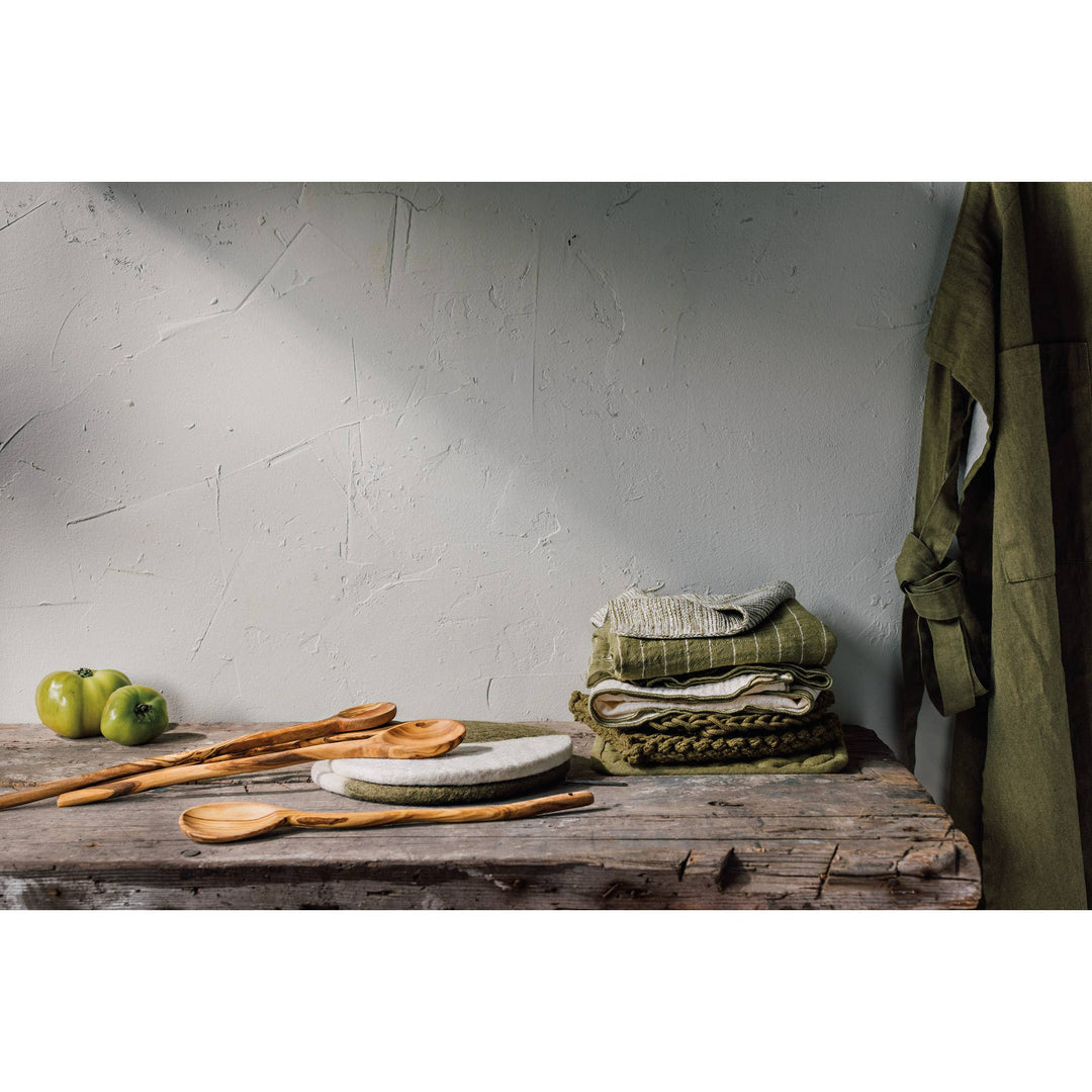 Wooden table with green apples, wooden spoons, and folded cloths against a textured wall.