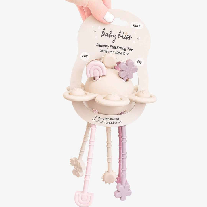 Baby bliss Sensory Pull String Toy in a pastel cream, pink, and lavender color scheme, held by a hand against a light gray background.