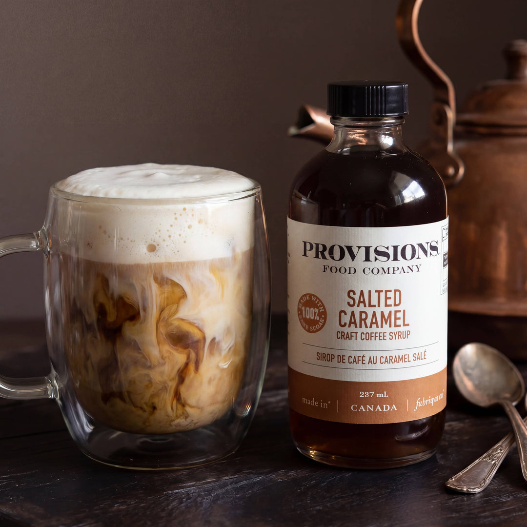 Bottle of Provisions Salted Caramel syrup next to a glass of iced coffee with a tea kettle in the background.