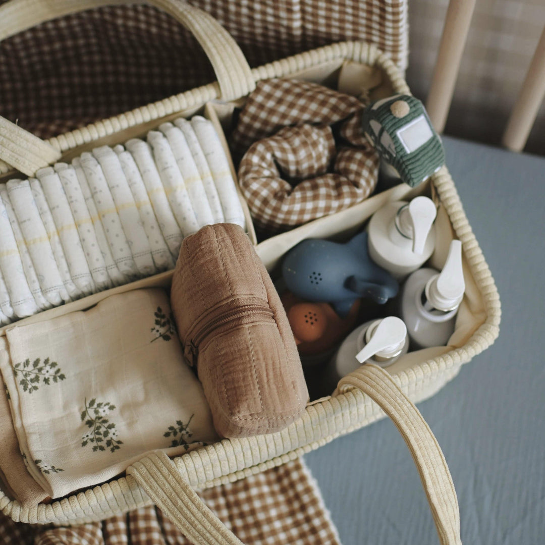 Woven basket with baby items including a toy, bottles, and cloth on a blue surface.
