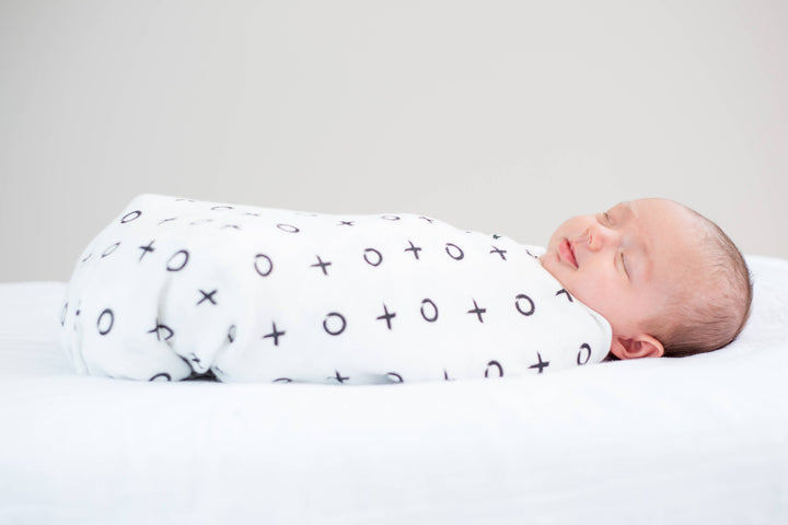 Newborn baby swaddled in a white blanket with black patterns on a light gray background