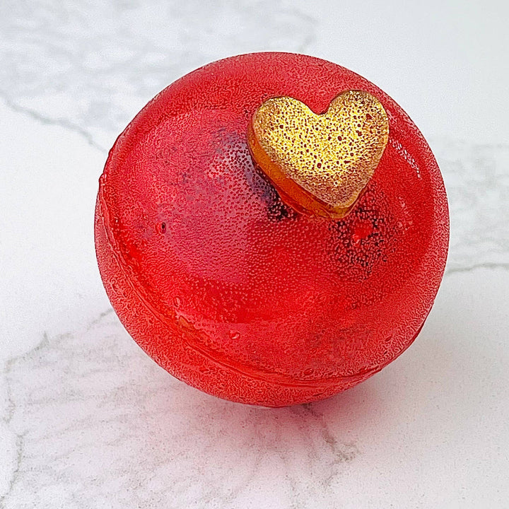 Red apple-shaped bath bomb with a gold heart on a marble surface