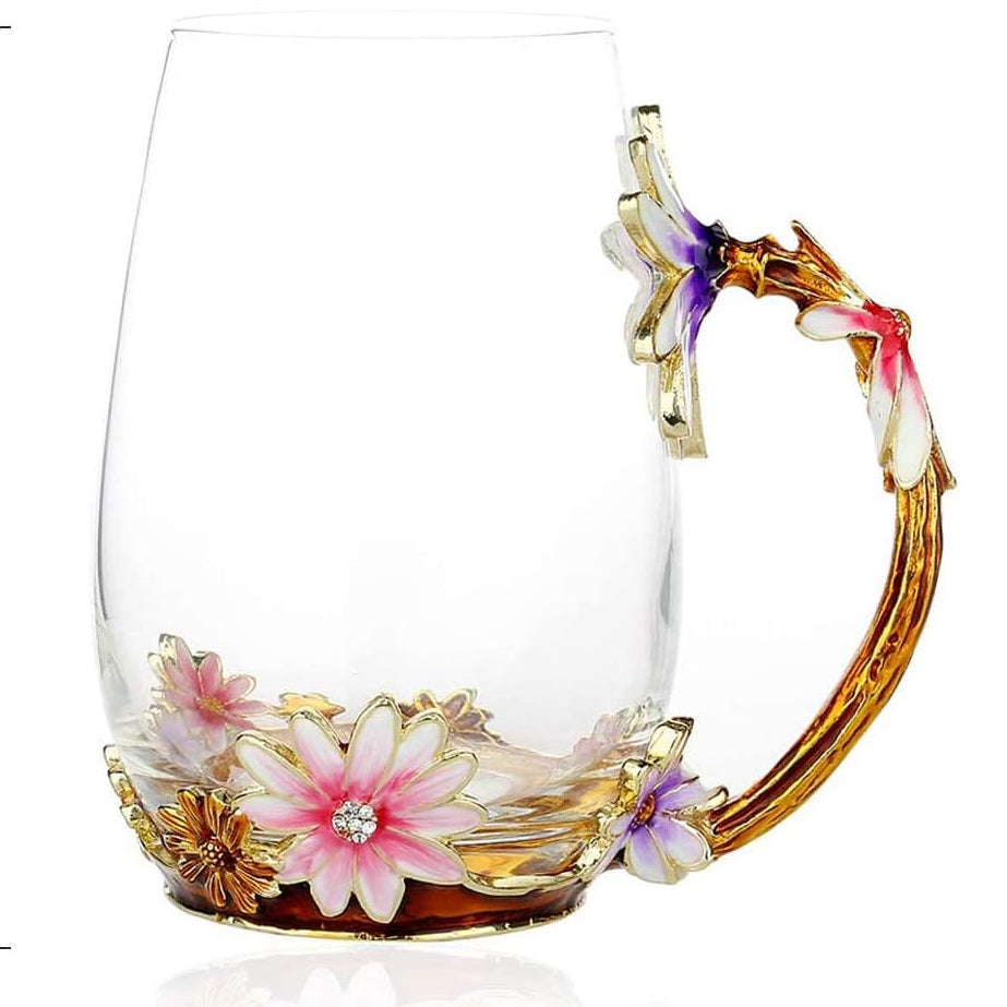 A clear glass mug with a gold-toned floral handle and pink, white, and purple enamel flowers at the base, shown alongside a red soda can for scale. The image includes dimension labels: 5.