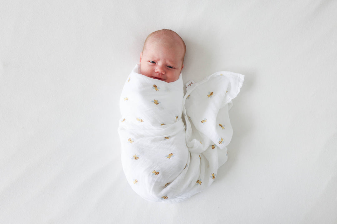 Newborn baby wrapped in a white swaddle with gold patterns on a light gray background