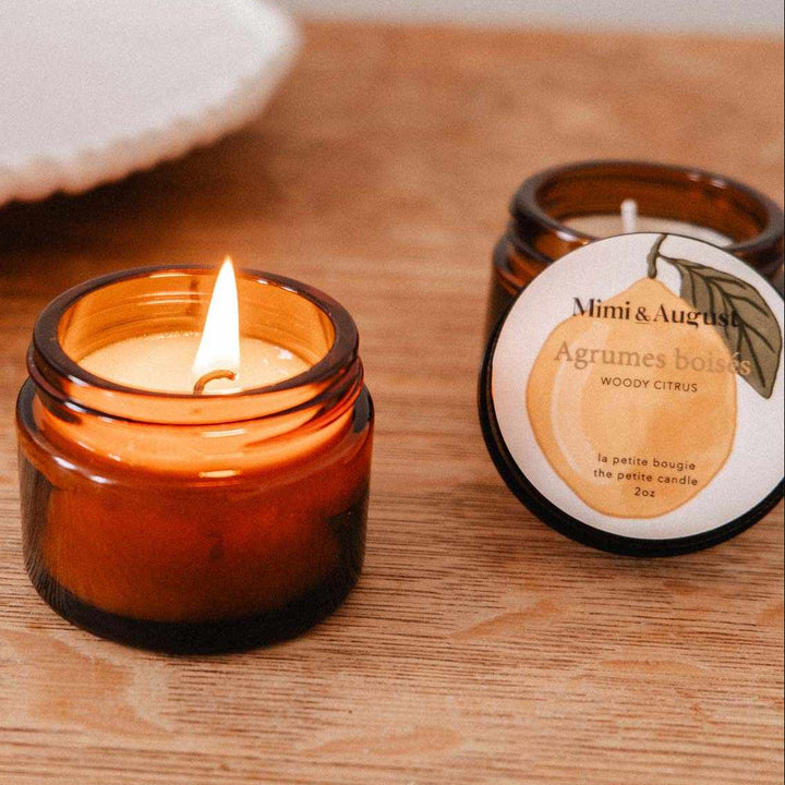 Candle in a glass jar on a wooden surface with another candle and a dish in the background.