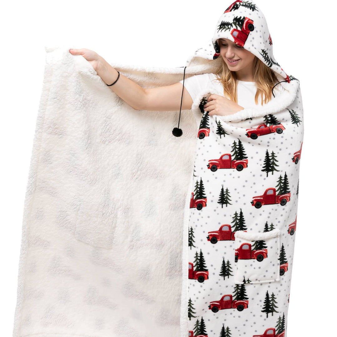 A woman wearing a white hooded blanket wrap with a red and black buffalo truck and pine tree pattern, holding up the fluffy white reverse side of the blanket against a white background.