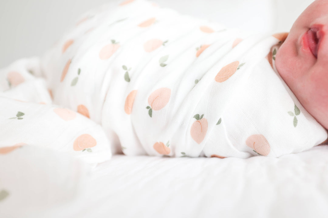Soft muslin cotton swaddle blanket with peach print for babies, by Lulujo Baby, shown folded with gentle fabric texture.