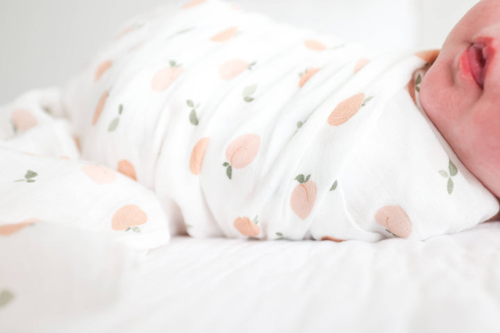 Soft muslin cotton swaddle blanket with peach print for babies, by Lulujo Baby, shown folded with gentle fabric texture.