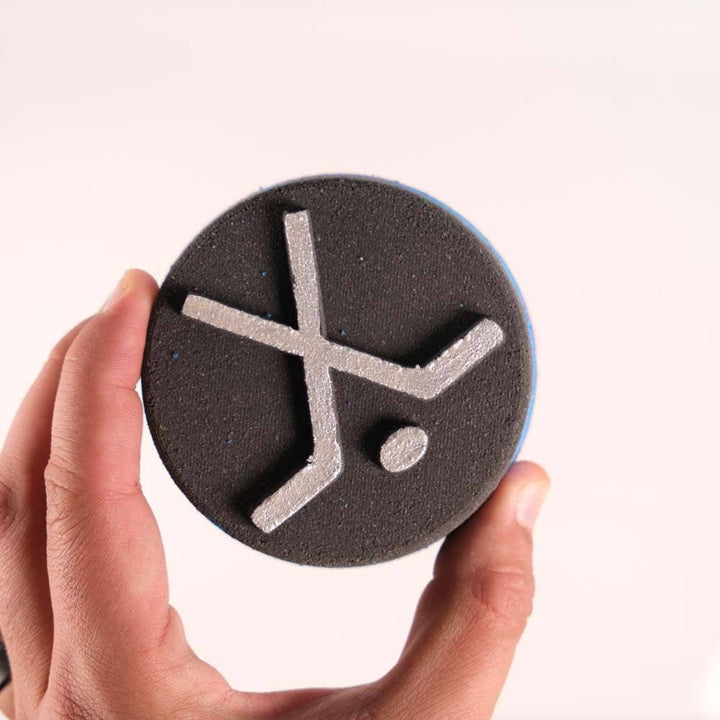 Bath bomb shaped like a hockey puck with a shoe charm, from Happy Hippo Bath, in a colorful, fizzy display.