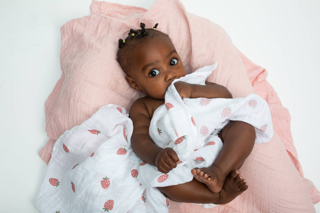 Two Lulujo Baby cotton swaddle blankets featuring strawberry and ballet slipper patterns, soft and breathable for infants.