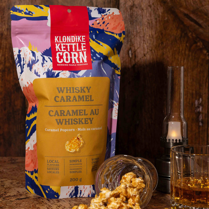 Klondike Kettle Corn Whisky Caramel package with popcorn and a glass of whiskey on a wooden surface.