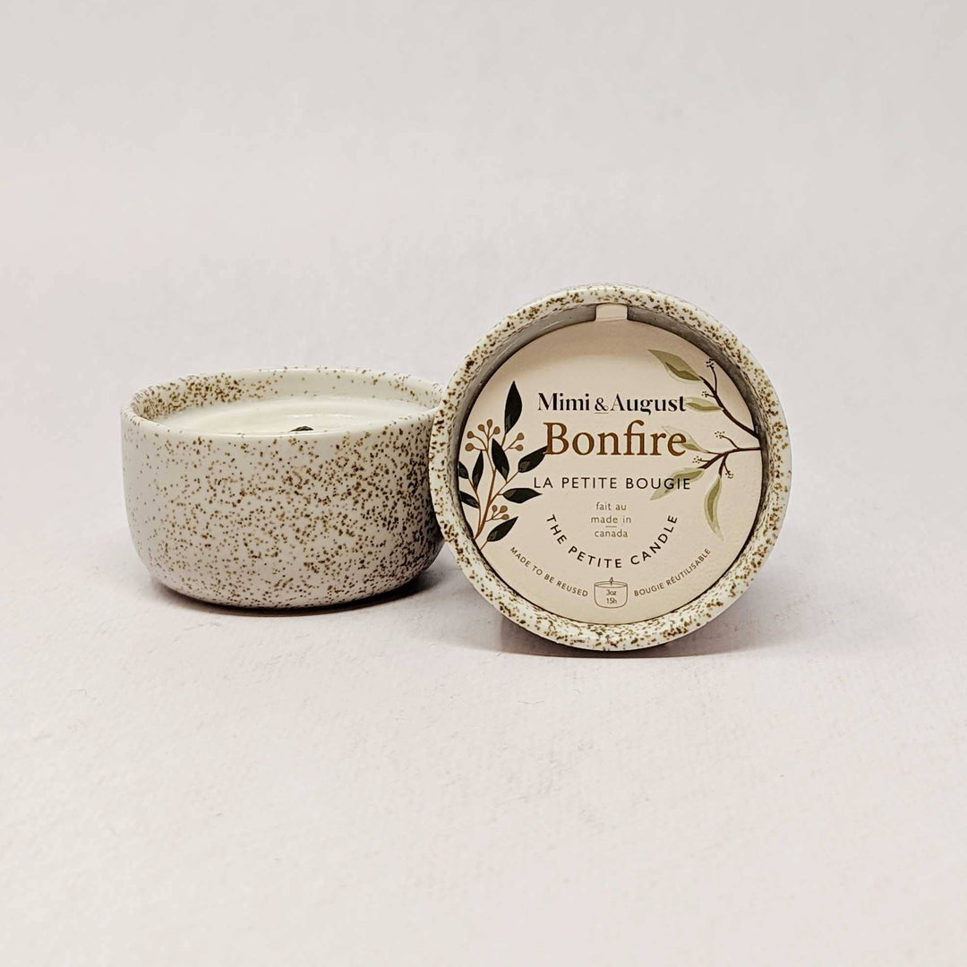 A small speckled ceramic candle jar with its lid placed beside it on a plain light background. The lid has printed text reading &