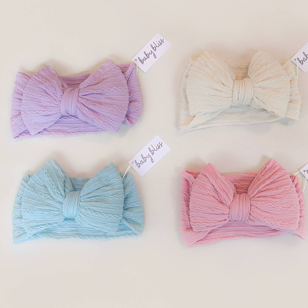 Four colorful headbands with bow designs on a beige background, each labeled &