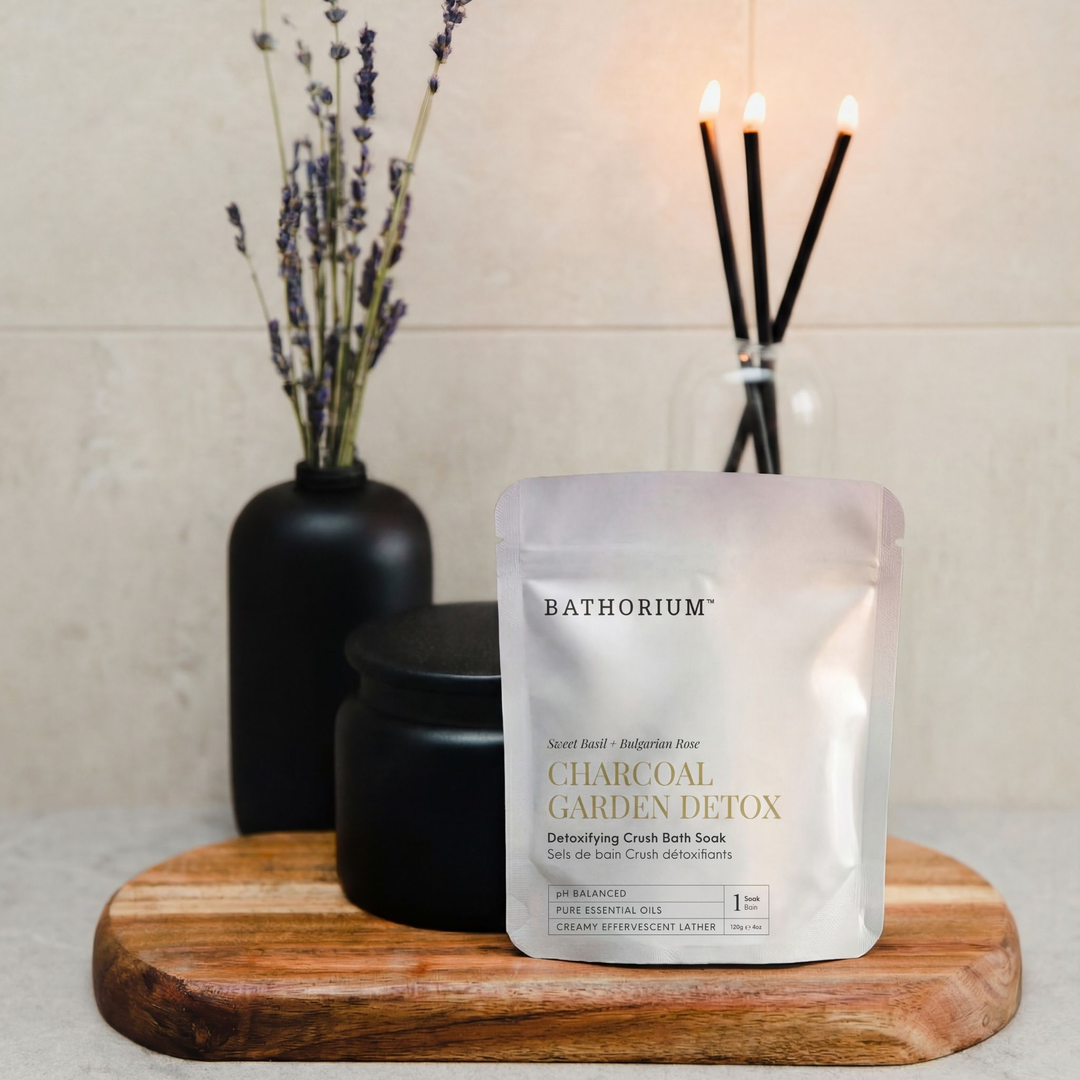 Bathorium Charcoal Garden Detox bath soaks on a wooden board with candles and lavender in the background.