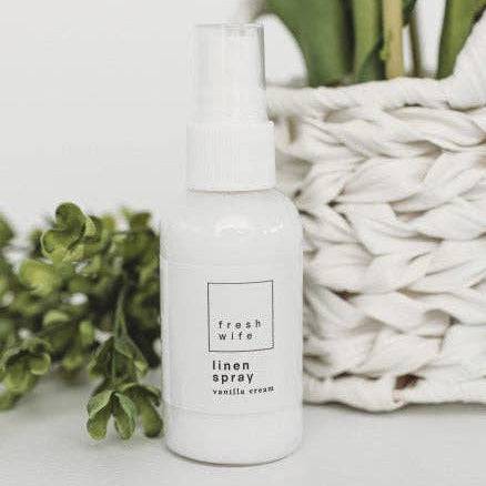 White linen spray bottle with greenery and a woven basket in the background