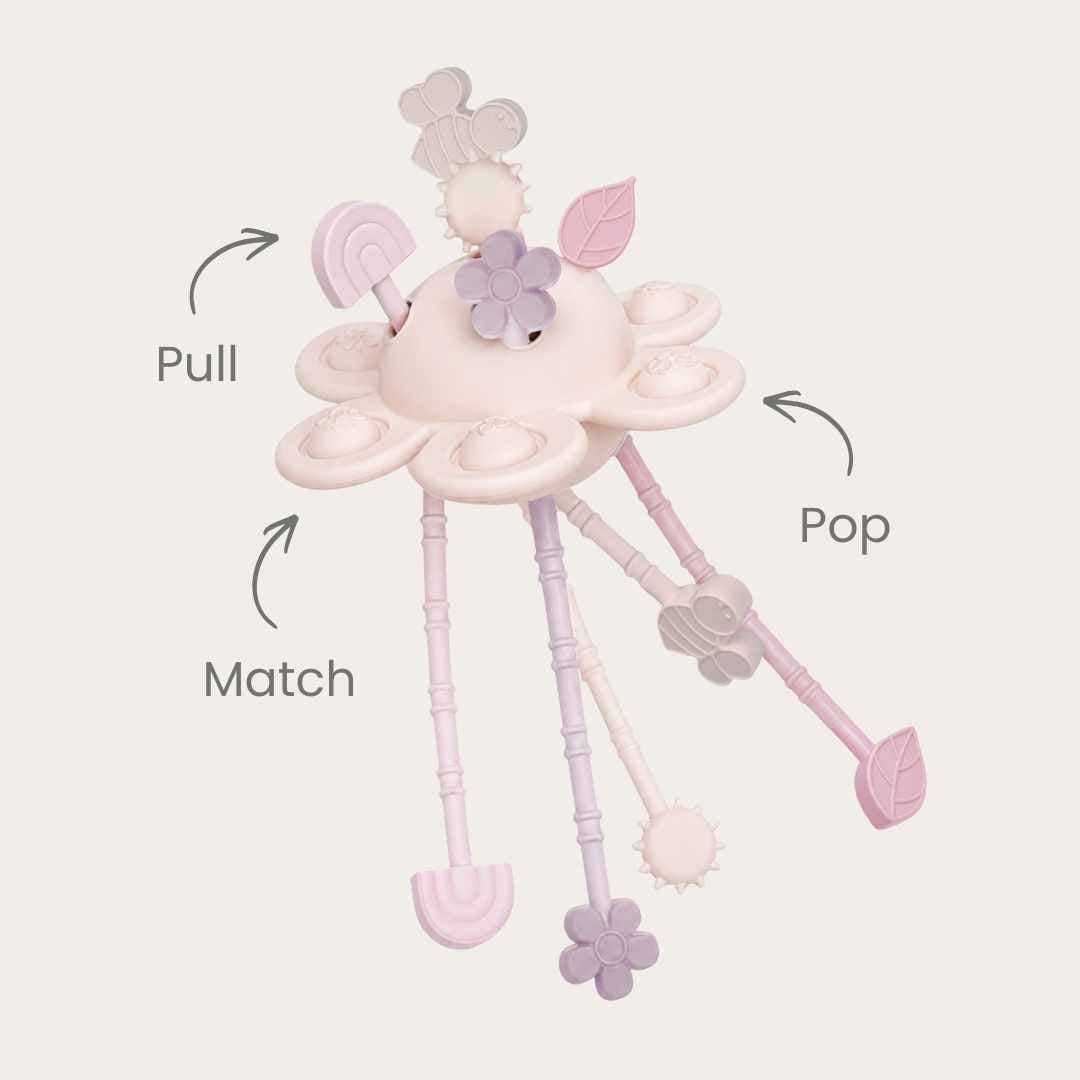 A pastel baby sensory toy with dangling tabs and printed callout arrows and labels reading &